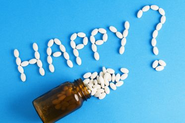 Word "happy" written whith pills on blue background. The photo is to convey a concept of excess medicines in modern life