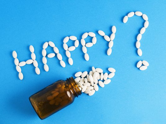 Word "happy" written whith pills on blue background. The photo is to convey a concept of excess medicines in modern life
