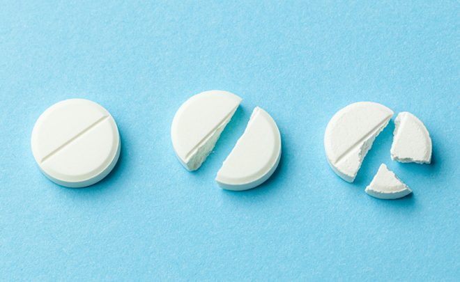 »Weiße Tabletten auf blauem Hintergrund. Wenige Tabletten zerbrochen in der Hälfte, wodurch die Dosis des Arzneimittels reduziert wurde.«